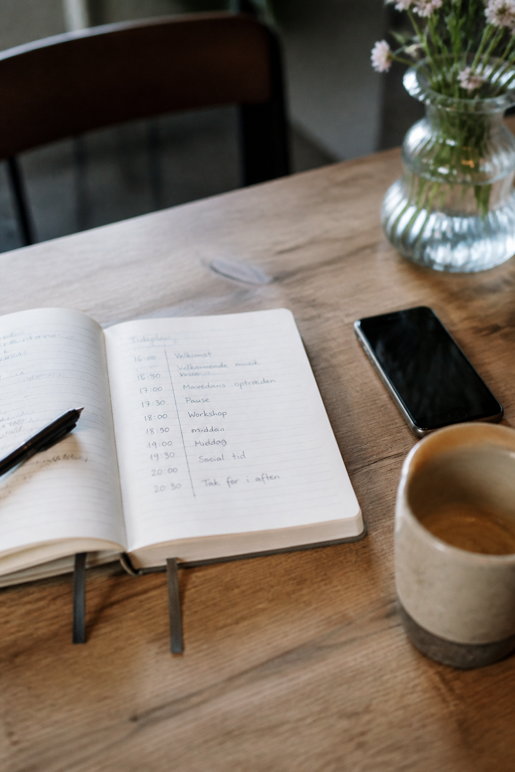 Opslået notesbog med en håndskrevet tidsplan ved siden af en telefon og en kop kaffe