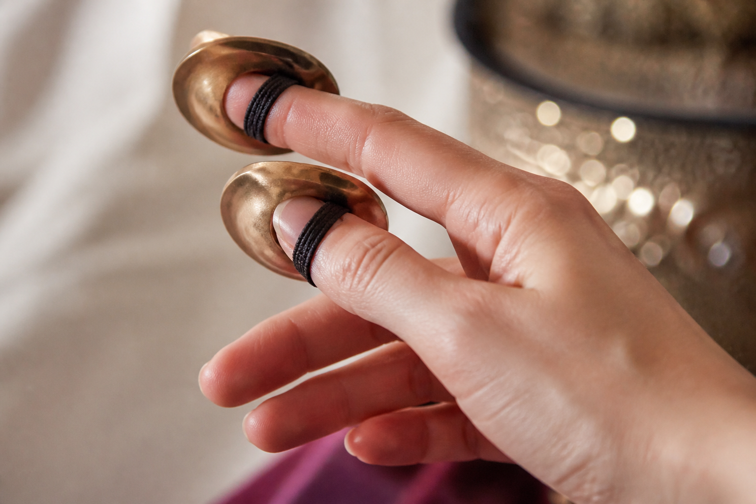 Nærbillede af et par messingfingercymbler spændt om fingrene med elastik